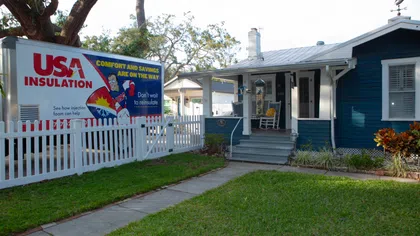 USA Insulation truck parked beside a blue house with white picket fence and green lawn on a sunny day.