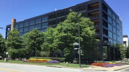 Modern black office building with large windows surrounded by trees and colorful flowerbeds on a sunny day