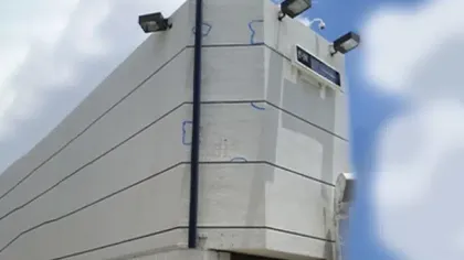 Large concrete corner structure with mounted lights under a partly cloudy blue sky