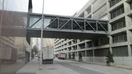 Urban street view with a pedestrian skybridge connecting two buildings above a narrow road with trucks parked.