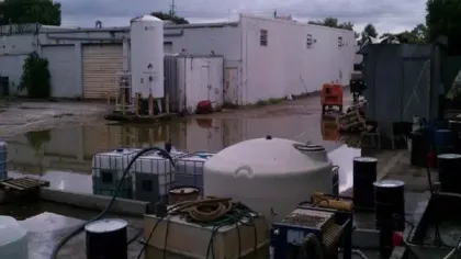 Industrial storage tanks and equipment outdoors with flooded ground and overcast sky at a facility.