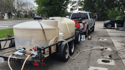 Pickup truck towing trailer with large water tanks, hoses, and pumping equipment near sewer access points.