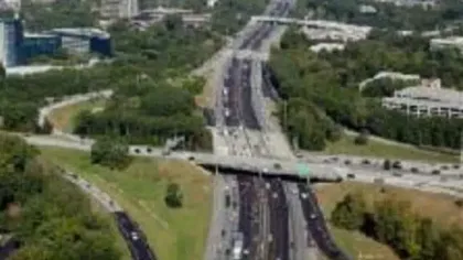 Aerial view of a multi-lane highway interchange surrounded by greenery and urban buildings on a clear day