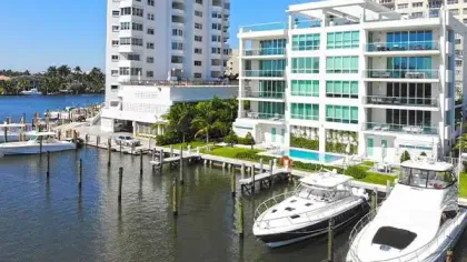 Marina with luxury yachts docked beside modern waterfront apartment buildings on a sunny day.