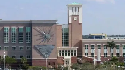Modern brick building with large clock tower and unique sunburst clock on facade under a clear blue sky.