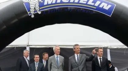 Group of six men in formal suits standing under a large Michelin arch at an event tent.