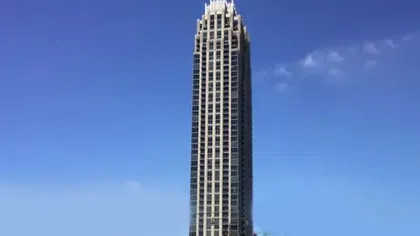 Tall modern skyscraper under a clear blue sky with detailed upper facade architectural features.