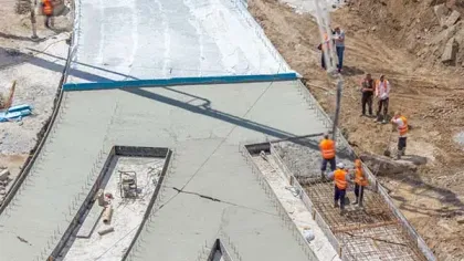 Construction workers pouring and smoothing concrete on a road under early development with rebar and dirt surroundings.