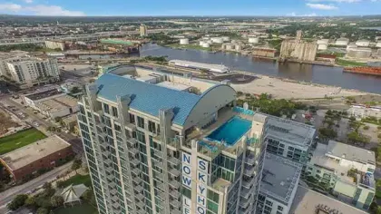 High-rise building with rooftop pool overlooking a river and cityscape under blue sky with clouds.