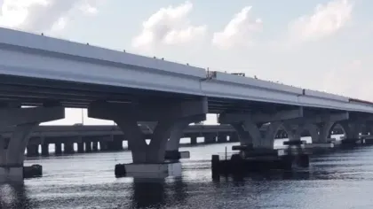 Concrete bridge structure spanning over calm water under a partly cloudy sky.