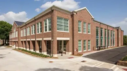 Two-story red brick institutional building with large glass windows under a blue sky with clouds.