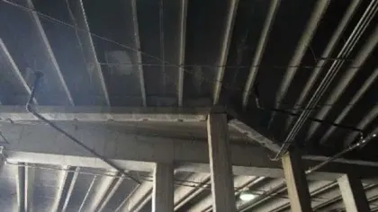 Concrete ceiling and beams in an industrial building with exposed pipes and lighting fixtures.