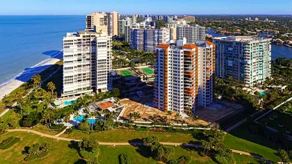 Aerial view of beachfront high-rise condos with pools, tennis courts, and green lawns near the ocean shore.