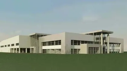 Modern commercial building with large windows, flat roof, and surrounding green lawn under clear sky