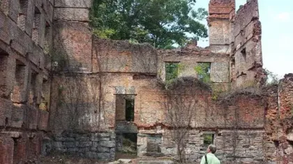 Person in green shirt exploring an old brick and stone building ruin overgrown with vegetation.