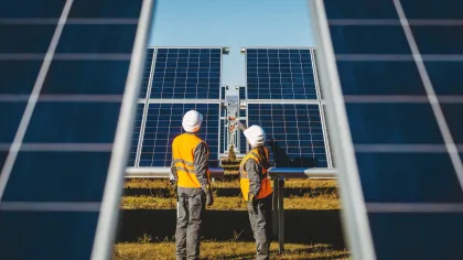 Two workers in orange safety vests and helmets inspecting solar panels in a solar farm on a sunny day
