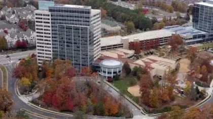 Aerial view of office buildings surrounded by autumn trees with red and orange foliage in an urban area.