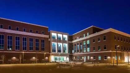 Modern three-story office building with large windows illuminated at night under a dark blue sky.