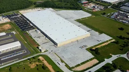 Aerial view of a large warehouse with surrounding parking and greenery in an industrial area.