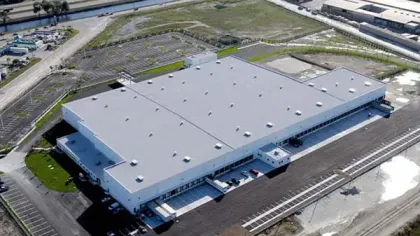 Aerial view of a large industrial warehouse with loading docks and ample parking areas surrounding it.