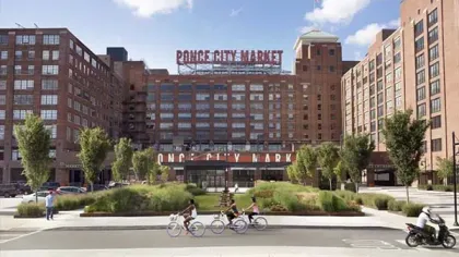 Exterior view of historic Ponce City Market with people biking and walking near green landscaping on a sunny day