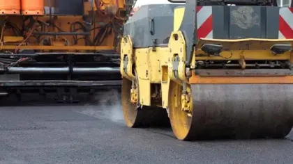 Close-up of a yellow asphalt roller compacting freshly laid black asphalt on road construction site.