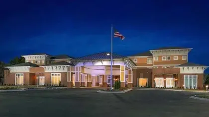 Modern brick building with covered entrance and American flagpole lit under a clear evening sky.