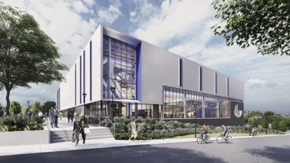 Modern white university building with large glass windows, people walking and biking outside on a sunny day.