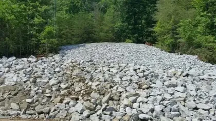 Rocky slope covered with large gray stones surrounded by dense green forest under a clear sky.