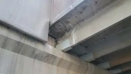 Close-up of a concrete bridge underside showing structural beams with water stains and wear.