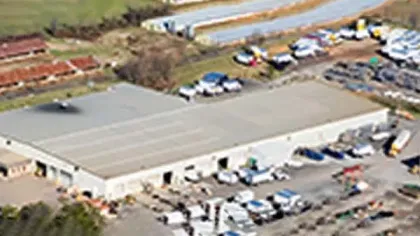Aerial view of a large warehouse surrounded by parked vehicles and storage areas in an industrial setting.
