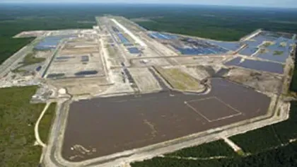 A large industrial site with multiple water-filled ponds and surrounding forest under a clear sky.