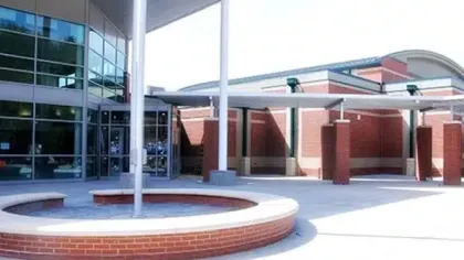 Modern school entrance with circular brick planter, glass windows, and covered walkways on a sunny day