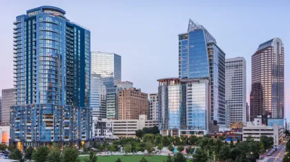 City skyline with modern glass skyscrapers and green parkland at dusk under clear sky.