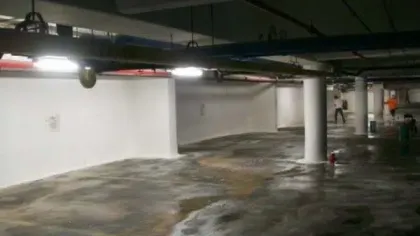 Empty underground parking garage with white walls and concrete floor, lit by overhead fluorescent lights.
