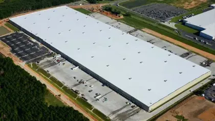 Aerial view of a large white-roofed industrial warehouse surrounded by parking lots and green space.
