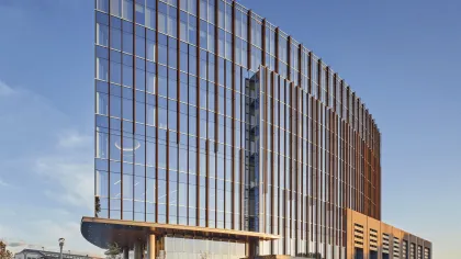 Modern curved glass office building with brown vertical panels and cars on the street in the evening light