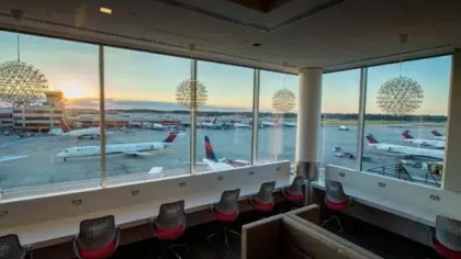 Airport lounge seating area with large windows overlooking planes on the tarmac at sunset.
