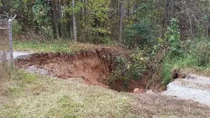 Large erosion area with exposed soil and collapsed ground near a fence and wooded area