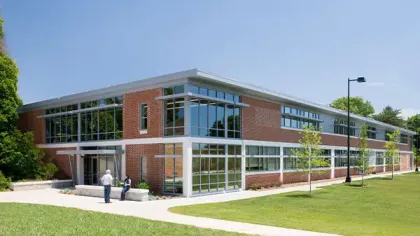 Modern two-story brick and glass commercial building with a green lawn and two people outside near the entrance.