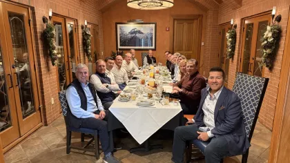 Group of people gathered around a long dining table in a cozy brick-walled room with festive decorations.