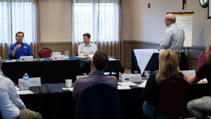 Business professionals engaged in a meeting with one presenter standing by a whiteboard in a conference room.