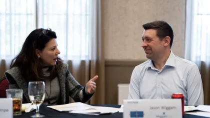 Two professionals engaged in a discussion at a conference table with documents and name tags in a meeting room.