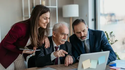 Three business professionals collaborating and discussing work on a laptop in a modern office setting.