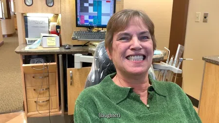 Smiling woman sitting in a dental chair in a dental office with equipment and monitor visible behind her