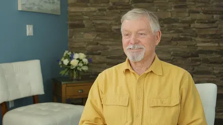 Smiling elderly man with gray hair and beard wearing yellow shirt against stone wall background