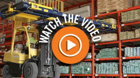 Forklift operating in warehouse with stacked pallets and shelves filled with goods behind it.