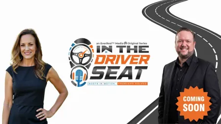 Two hosts stand beside the In The Driver Seat logo with a road and Coming Soon badge on white background.