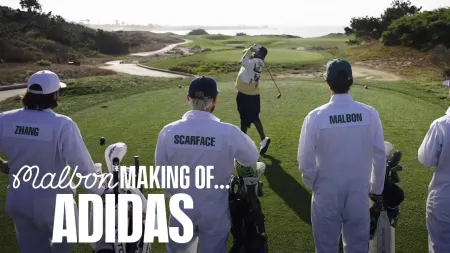 Golfers in white Malbon caddie outfits watching a player tee off on a sunny coastal golf course.