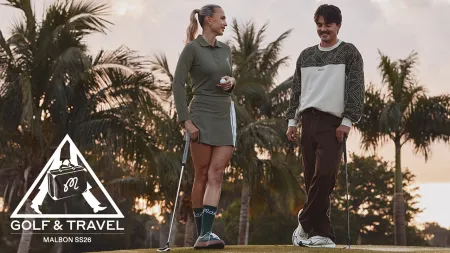 Man and woman standing on golf course with clubs, palm trees, and sunset background during golf and travel event.